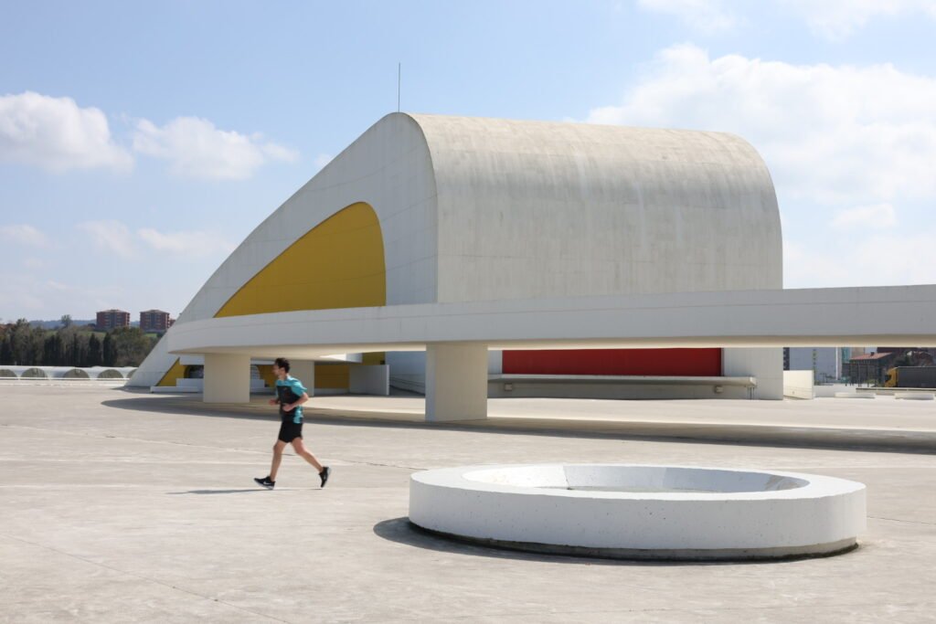 Edificio blanco curvo con interior amarillo y una persona caminando por la plaza