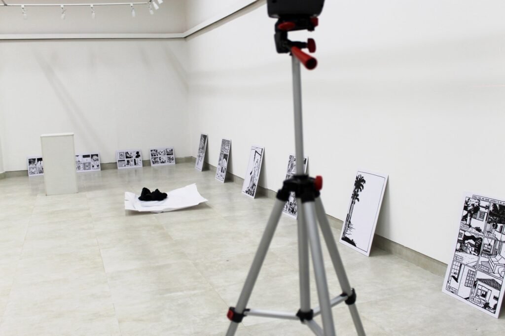 Montaje de una exposición: nivel láser sobre trípode en una sala vacía, con las obras apoyadas en la pared