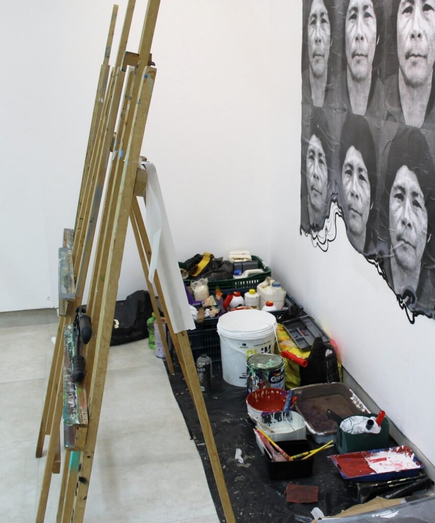 Montaje de una exposición: caballetes, botes de pintura y pinceles sobre una lona junto a la pared