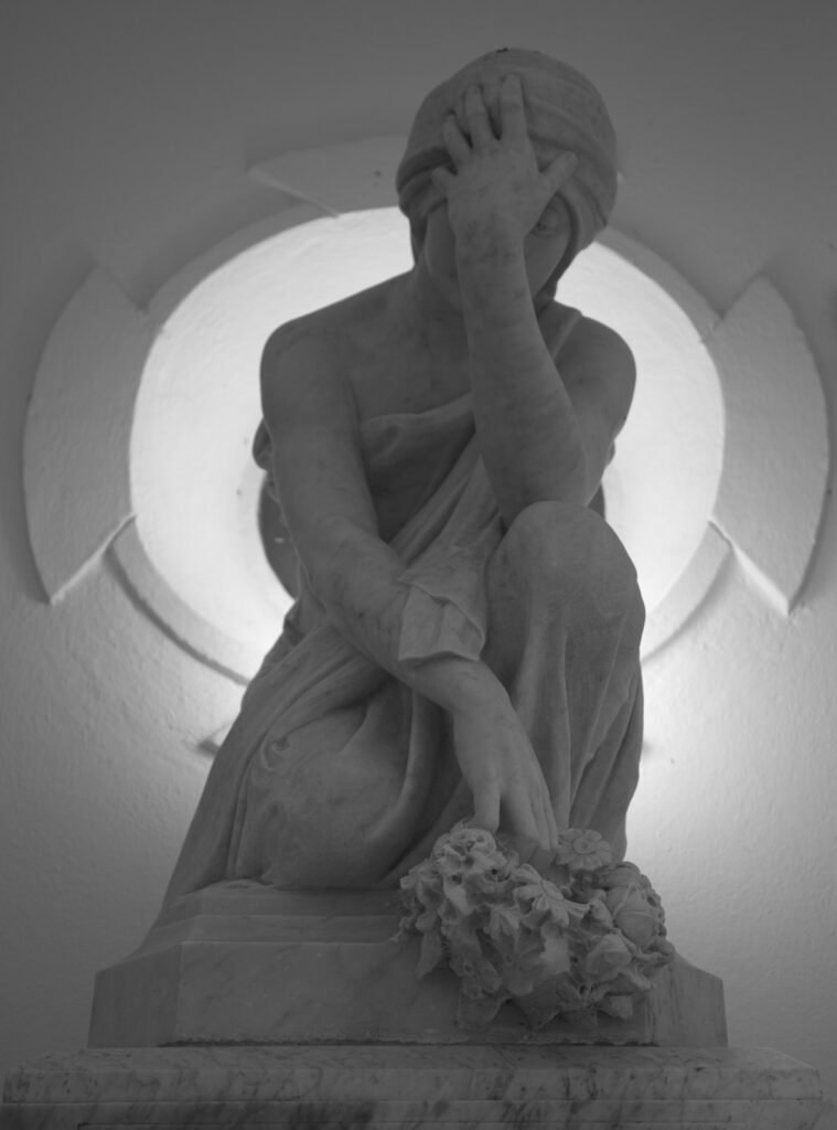Estatua de una figura sentada con la mano en el rostro, a contraluz