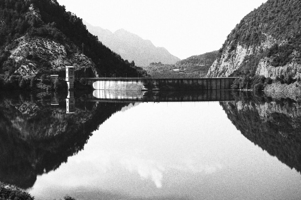 Montañas y presa reflejadas en un embalse, en blanco y negro